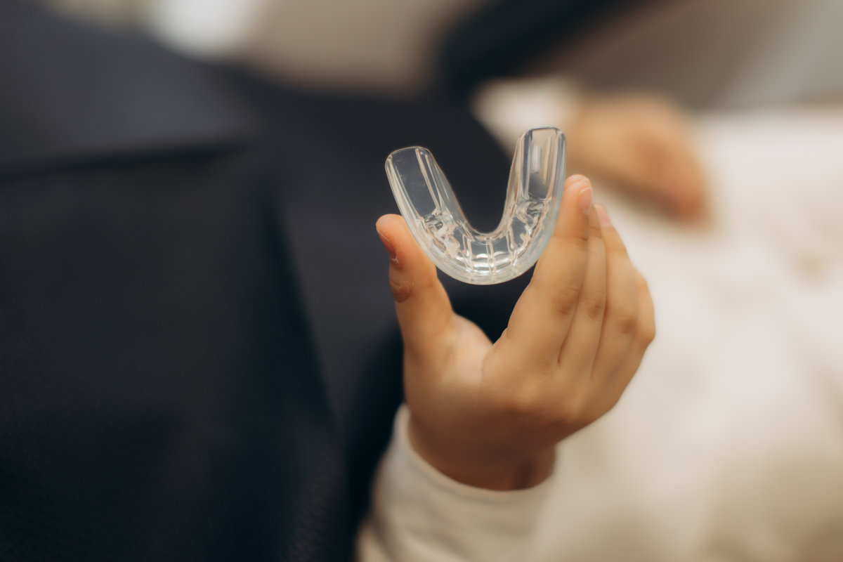 Hand holding a transparent dental guard, emphasizing the importance of dental care and protection for oral health and wellness